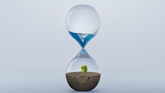 Hourglass with fresh water dropping to green plant planting on dry land