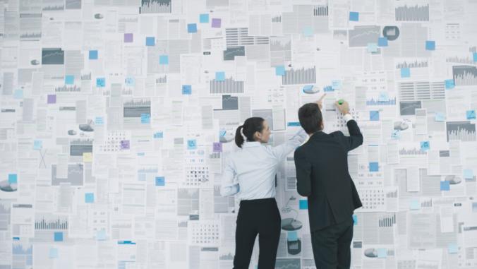  Corporate executives planning their business strategy: they are analyzing many financial reports and charts hanging on a wall