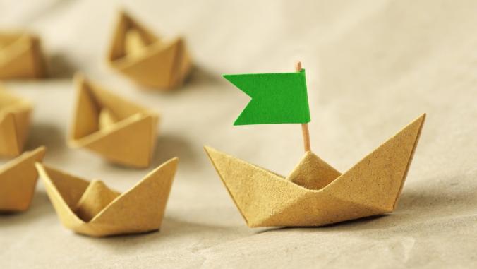 Origami recycled paper boat with green flag leading a group of small boats (leadership concept)