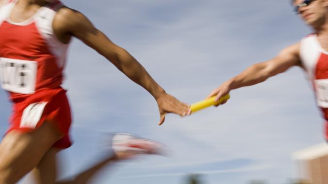 A blurred photo of 2 runners attempting to pass a relay baton